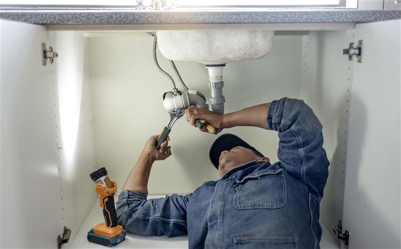 Plumber repairing pipes beneath a bathroom sink in Belmont